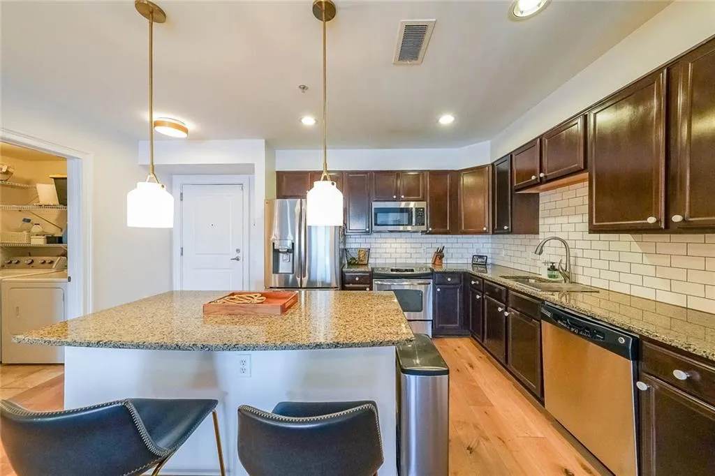 Kitchen featuring a sink, light wood-style floors, washer / dryer, appliances with stainless steel finishes, and a kitchen island