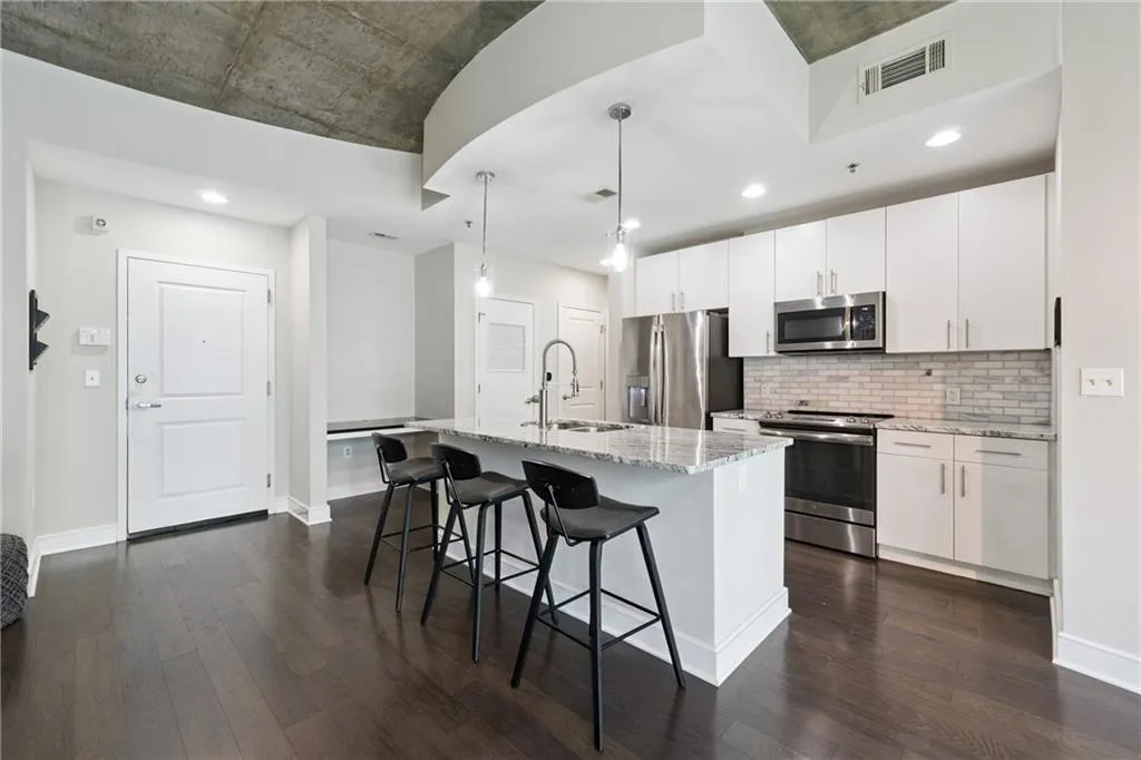 Kitchen with appliances with stainless steel finishes, dark wood finished floors, a breakfast bar area, white cabinets, and recessed lighting