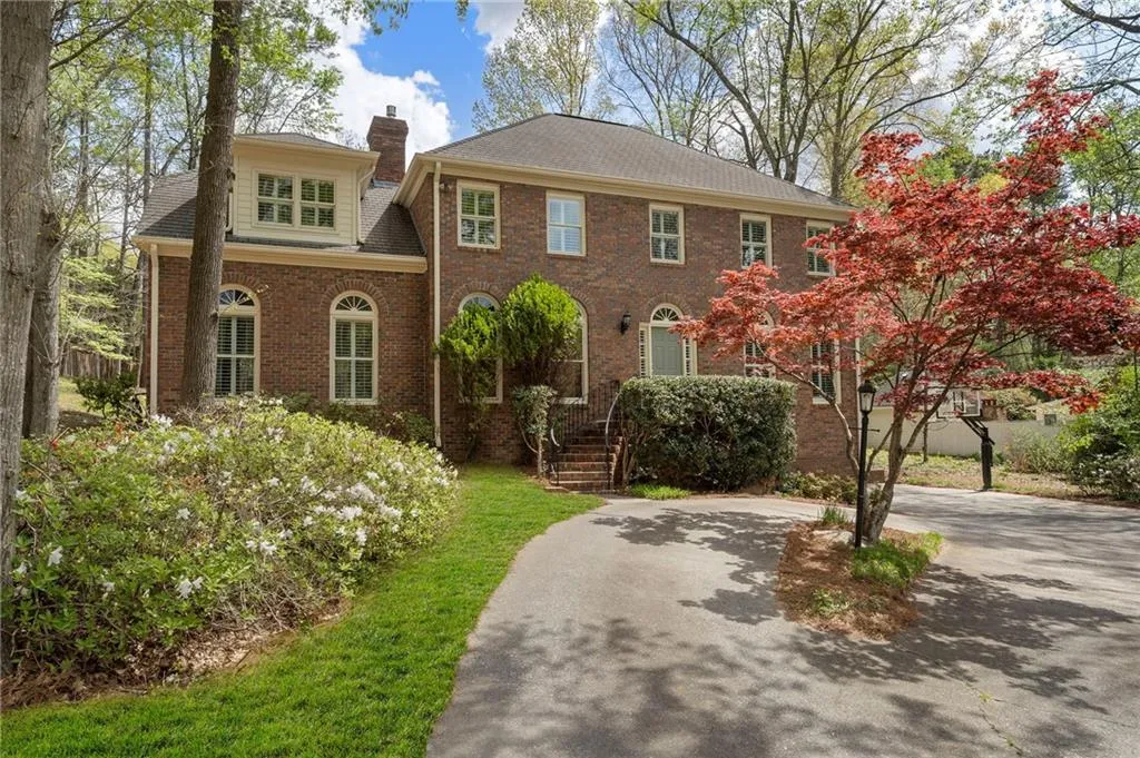 View of front facade featuring brick siding, driveway, a chimney, and a shingled roof