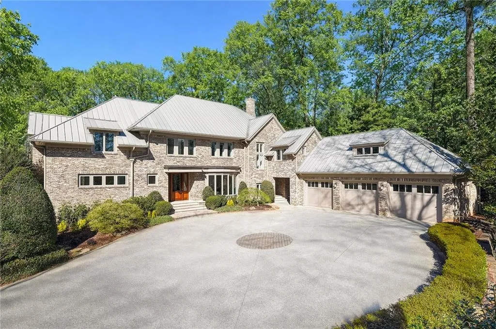 View of front of house with a standing seam roof, driveway, stone siding, a chimney, and an attached garage
